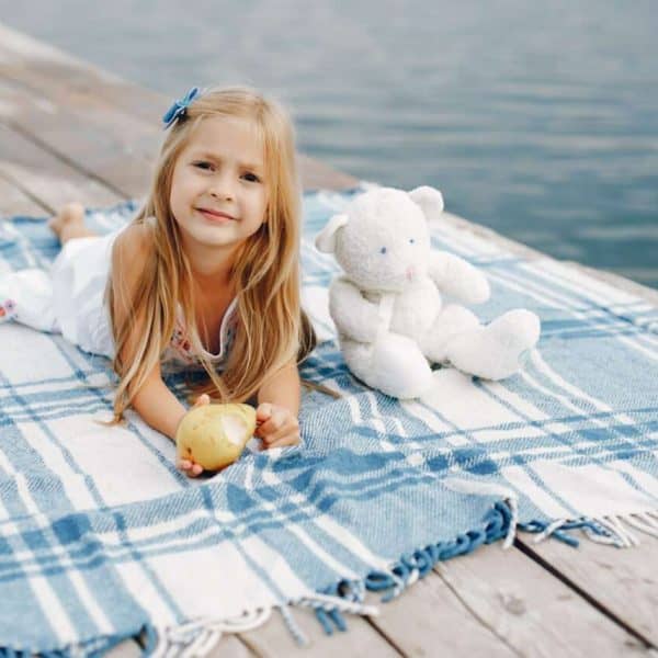 Cute little girl in a white dress. Child sitting near water.